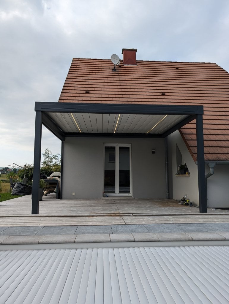 Réalisation pergola bioclimatique - Pergola bioclimatique à lames orientables - Modèle Rayy XL - Largeur 4,15m x avancé 3,5m - Couleur structure Gris Anthracite RAL 7016 Sablé - Couleur lames Blanc RAL 9016 Satiné - Option store zip motorisé toile Mermet screen 5500 référence 0102 gris blanc et trois lames avec LEDS intégrées