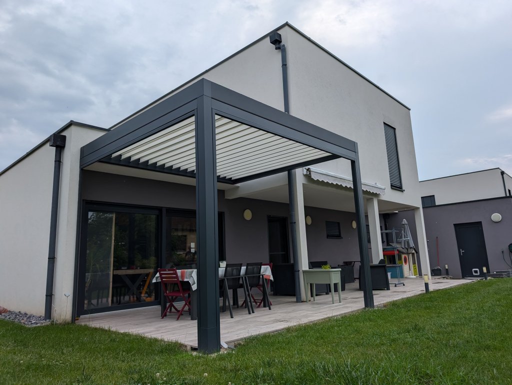 Réalisation pergola bioclimatique - Pergola bioclimatique à lames orientables - Modèle Rayy XL - Largeur 4,15m x avancé 3,5m - Couleur structure Gris Anthracite RAL 7016 Sablé - Couleur lames Blanc RAL 9016 Satiné - Option store zip motorisé toile Mermet screen 5500 référence 0102 gris blanc et trois lames avec LEDS intégrées